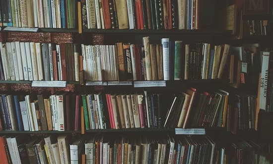 Biblioteca universitária com estantes de livros e estudantes ao fundo