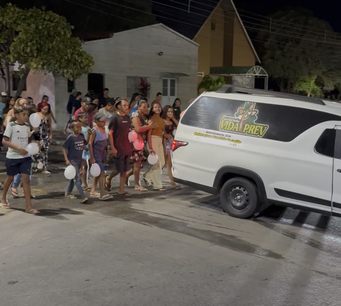Cortejo fúnebre à noite em Delmiro Gouveia com pessoas segurando balões brancos em sinal de paz