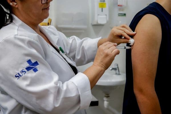 Seringa e frasco de vacina sobre fundo azul, representando a importância da imunização em adultos