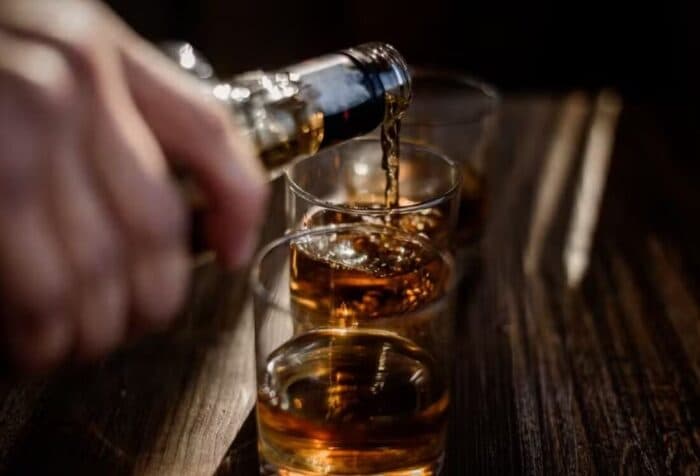 Bebida alcoólica em copo sobre mesa com fundo desfocado, representando alerta sobre bebidas adulteradas com metanol
