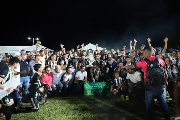Jogadores de futebol amador comemorando título em campo com troféu
