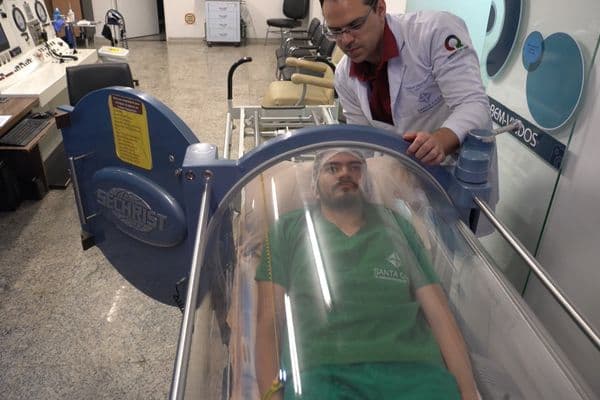 Câmara hiperbárica cilíndrica em ambiente hospitalar, com paciente recebendo oxigenoterapia