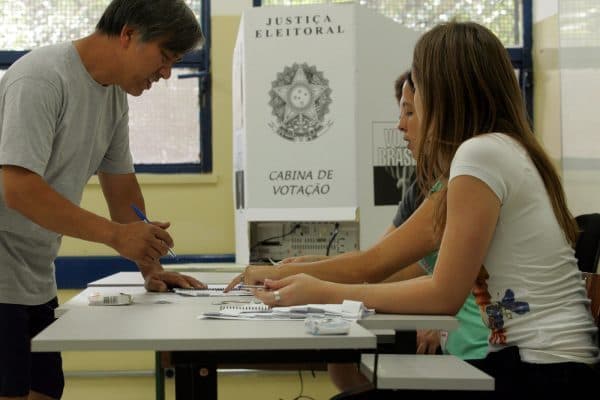 Mesário auxilia eleitor em seção eleitoral durante eleições no Brasil