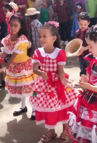 Crianças em trajes típicos juninos dançando quadrilha em pátio escolar no sertão alagoano