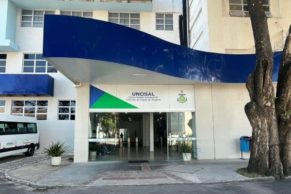 Fachada de universidade estadual de saúde com estudantes em área externa