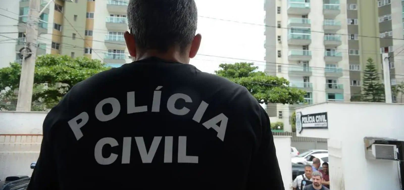 Policiais durante operação de busca e apreensão com viaturas ao fundo