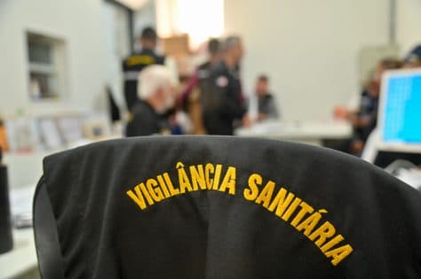 Fiscal da Vigilância Sanitária com colete azul e crachá de identificação durante inspeção