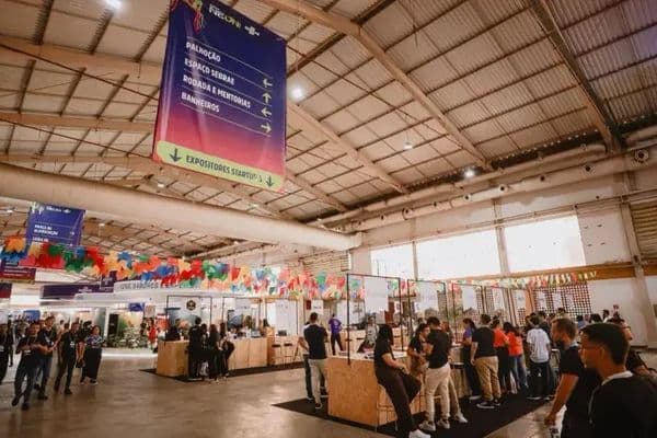 Espaço de startups no NEON 2026, em Maceió, com estandes expositores e visitantes circulando