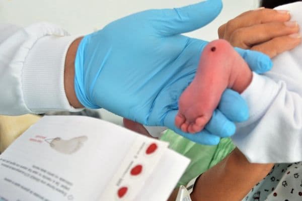 Profissional de saúde realizando a coleta do Teste do Pezinho em recém-nascido