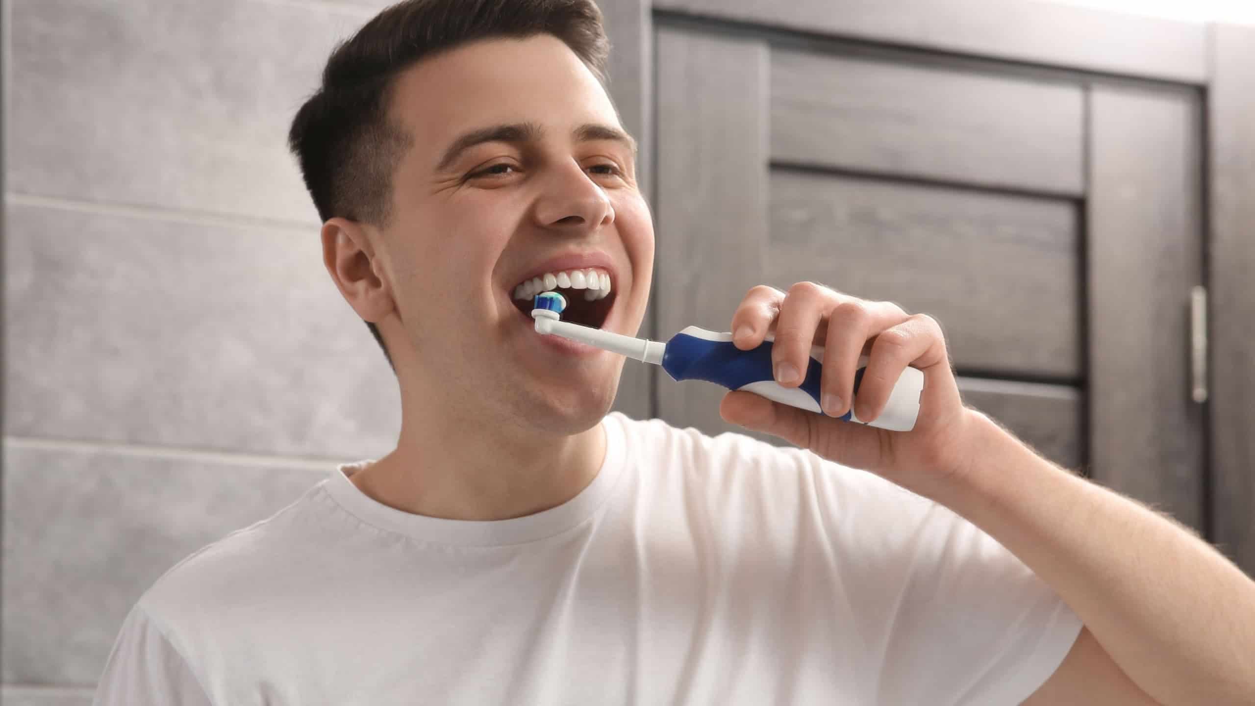 Homem escovando os dentes com escova elétrica no banheiro / Crédito: New Africa (Shutterstock/reprodução)