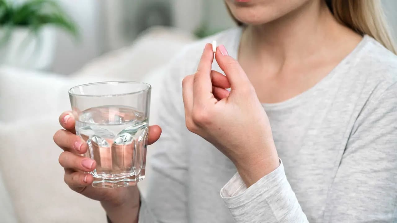 Mulher com um remédio e copo de água / Crédito: brizmaker(shutterstock/reprodução)
