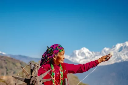 Idosa Nepalesa Tecendo Algodão Em Um Dia Ensolarado, Com A Cordilheiraannapurna, No Nepal, Ao Fundo. - Imagem: Shutterstock/Keshav Dulal